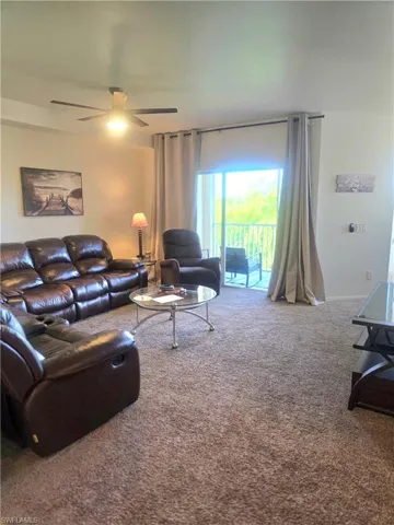 Living area with carpet floors and ceiling fan with sliding door entrance to screened patio