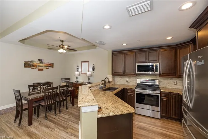 Kitchen featuring dark wood finish cabinetry, stainless steel appliances, a raised ceiling, a ceiling fan, and light stone countertops