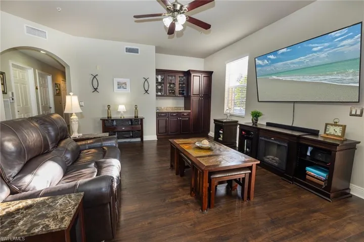 Living area with dark wood-type flooring, ceiling fan, and arched walkways