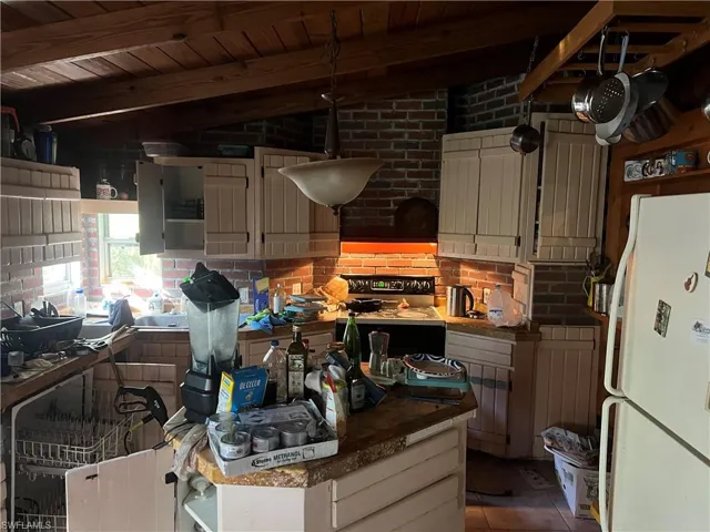 Kitchen with white appliances, white cabinets, vaulted ceiling with beams, wood ceiling, and brick wall