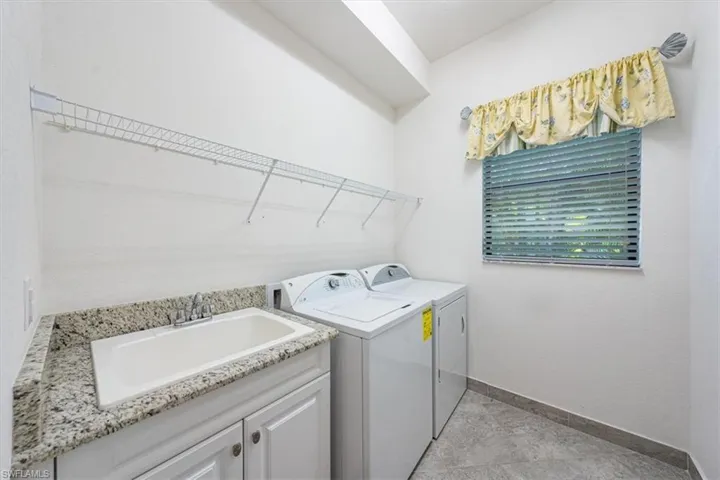 Clothes washing area with light tile patterned floors, washer and dryer, and sink