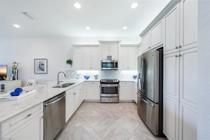 Kitchen featuring tasteful backsplash, light stone counters, stainless steel appliances, sink, and white cabinets