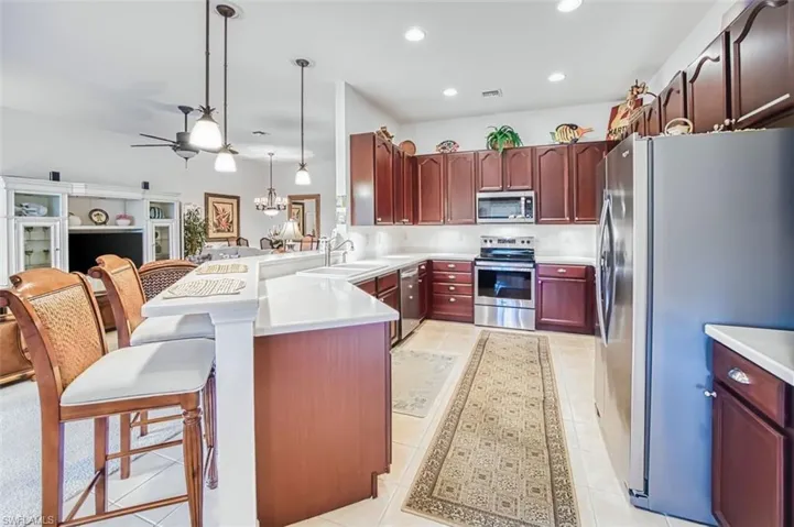 Kitchen with stainless steel appliances, ceiling fan, a kitchen bar, a peninsula, and bold wood finish cabinetry