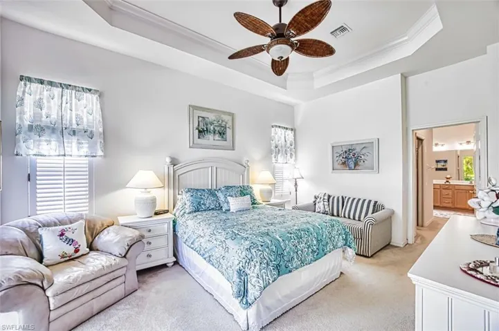 Bedroom with carpet, ensuite bathroom, crown molding, a tray ceiling, and a ceiling fan
