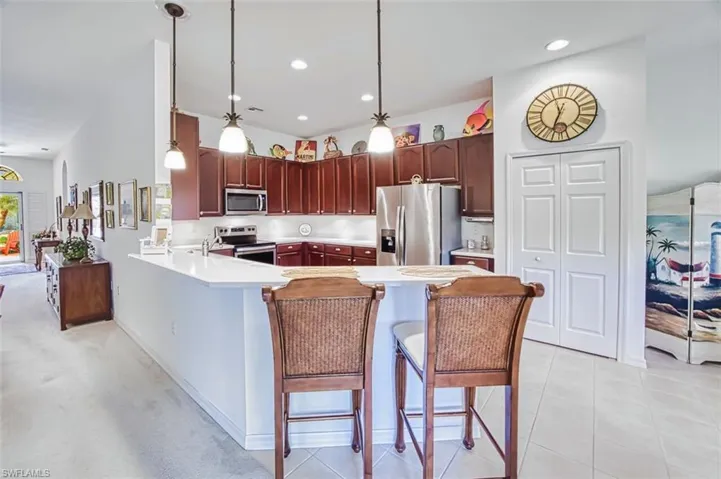 Kitchen featuring a peninsula, stainless steel appliances, a kitchen bar, hanging light fixtures, and light stone countertops