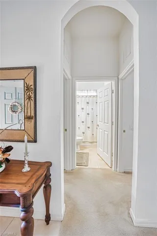 Hallway featuring arched walkways, light colored carpet, and a textured wall