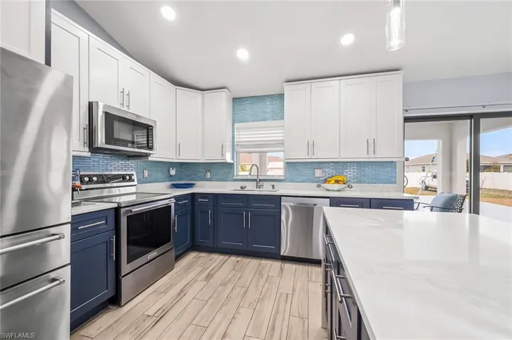 Kitchen featuring two tone cabinets, stainless steel appliances, light wood-style floors, light stone countertops, and backsplash