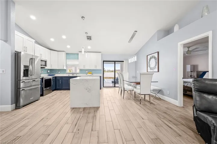 Kitchen with lofted ceiling, hanging light fixtures, stainless steel appliances, dual tone cabinetry, and light wood-style flooring