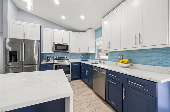 Dual tone kitchen featuring two tone cabinets, vaulted ceiling, stainless steel appliances, light stone counters, and recessed lighting