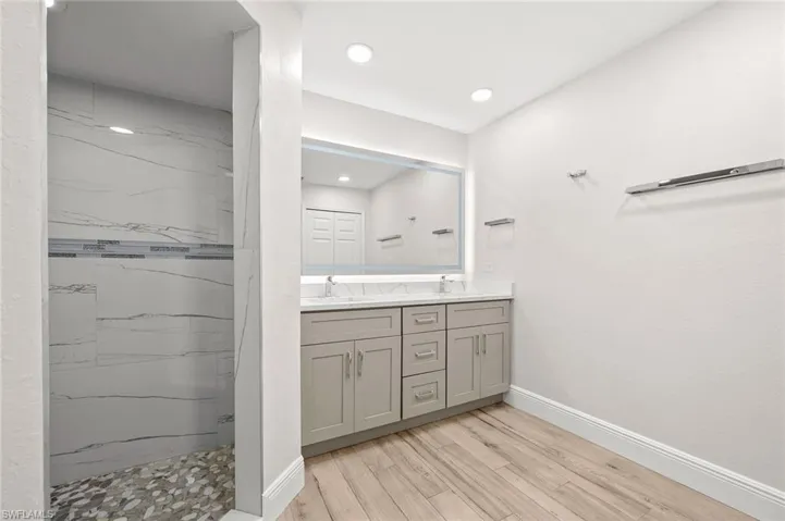 Full bathroom featuring a marble finish shower, double vanity, light wood-style flooring, and recessed lighting