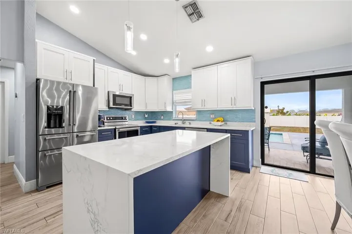 Two tone kitchen featuring two tone color scheme, stainless steel appliances, lofted ceiling, tasteful backsplash, and wood tiled floors