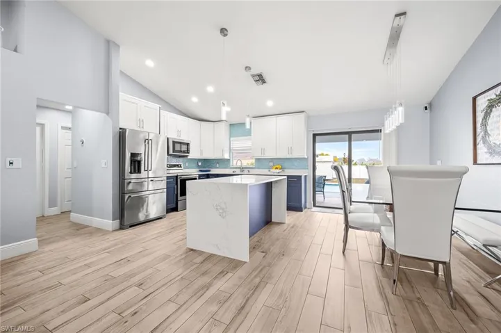 Two tone kitchen featuring lofted ceiling, stainless steel appliances, pendant lighting, a center island, and wood tiled floors