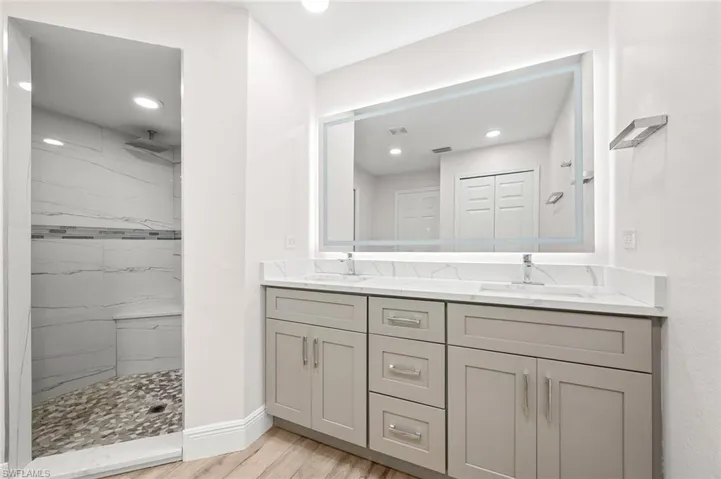 Full bath featuring double vanity, a marble finish shower, and light wood-style flooring