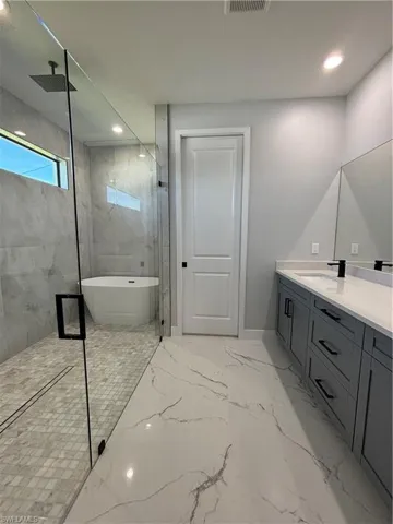 Full bathroom featuring a soaking tub, porcelain finish floor, vanity, a walk in shower, and recessed lighting
