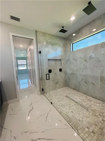 Bathroom with porcelain finish floor, a marble finish shower, visible vents, and baseboards