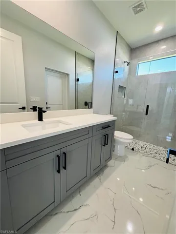 Bathroom featuring visible vents, toilet, marble finish floor, vanity, and a shower stall