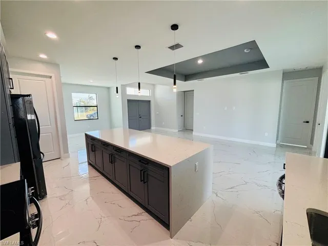 Kitchen featuring porcelain finish floor, a raised ceiling, visible vents, hanging light fixtures, and freestanding refrigerator