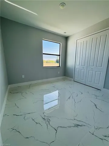Unfurnished bedroom featuring porcelain finish floor, a closet, and baseboards