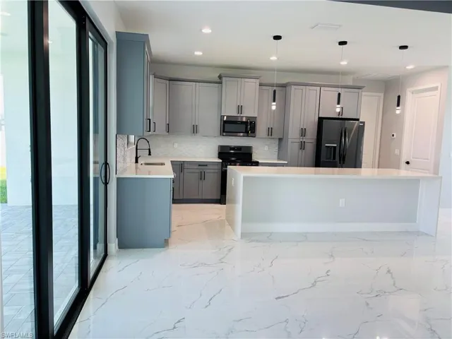 Kitchen featuring appliances with stainless steel finishes, light countertops, decorative light fixtures, and gray cabinetry