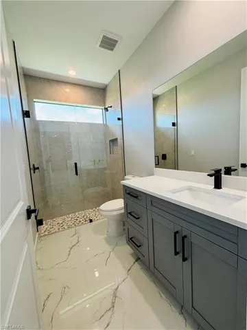 Full bathroom featuring toilet, vanity, visible vents, porcelain finish floor, and a shower stall