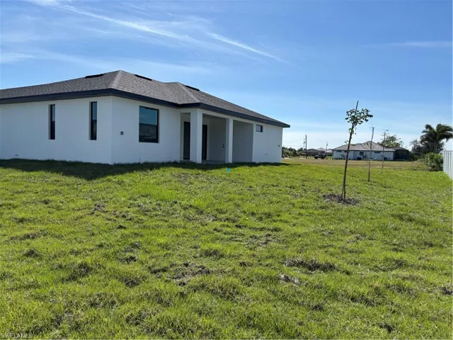 Rear view of house featuring roof with shingles, a lawn, and stucco siding