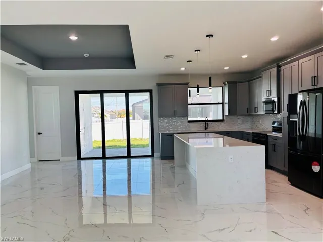 Kitchen with a center island, light countertops, black appliances, pendant lighting, and a sink