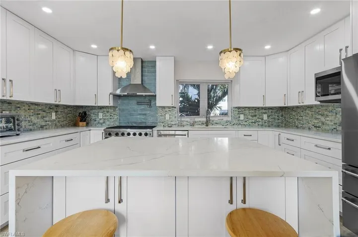Kitchen featuring light stone counters, hanging light fixtures, white cabinets, and recessed lighting