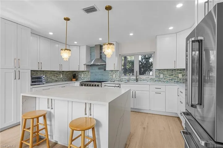 Kitchen featuring freestanding refrigerator, light stone counters, a kitchen bar, white cabinetry, and wall chimney range hood