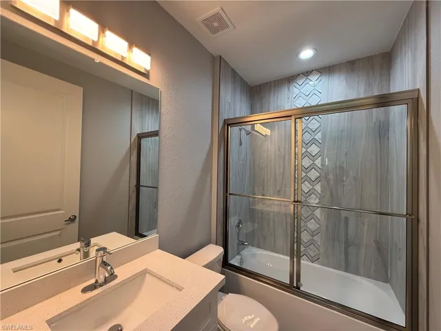 Full bathroom with toilet, vanity, and combined bath / shower with glass door