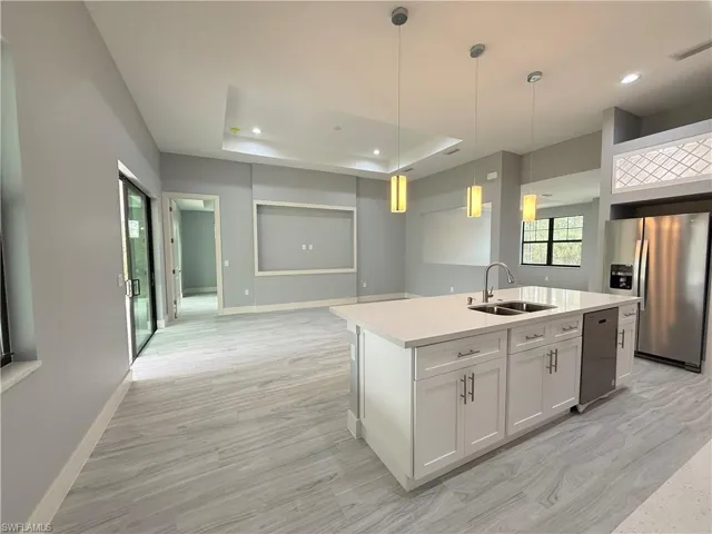 Kitchen with white cabinets, a center island with sink, stainless steel fridge, sink, and decorative light fixtures