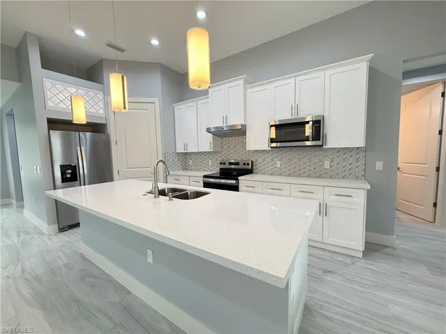 Kitchen with appliances with stainless steel finishes, pendant lighting, white cabinets, and sink