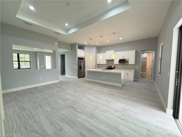 Kitchen with stainless steel appliances, white cabinets, decorative light fixtures, an island with sink, and decorative backsplash