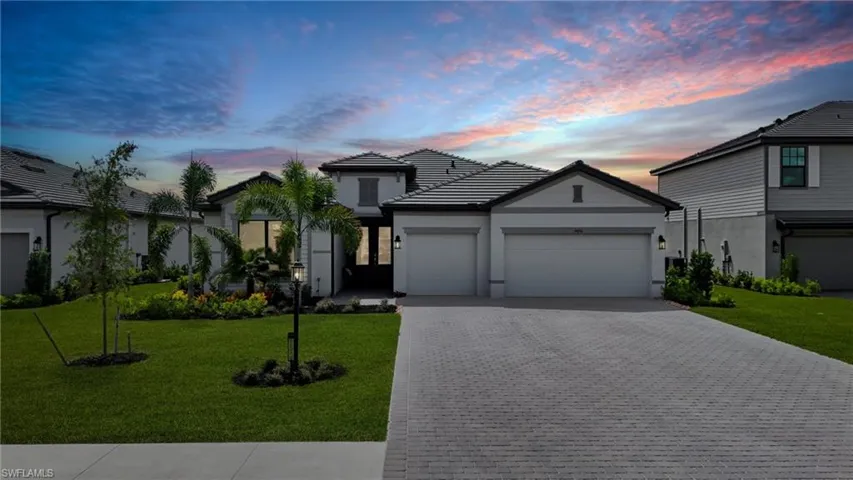 View of front facade featuring a front lawn, decorative driveway, a garage, stucco siding, and a tiled roof