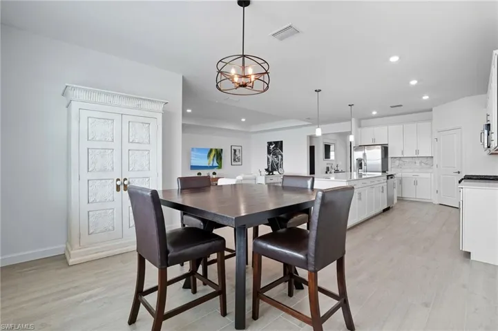 Dining area with light wood-style flooring, a chandelier, recessed lighting, and a raised ceiling
