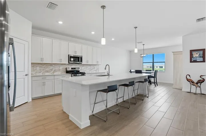 Kitchen featuring a kitchen breakfast bar, a kitchen island with sink, pendant lighting, white cabinetry, and recessed lighting