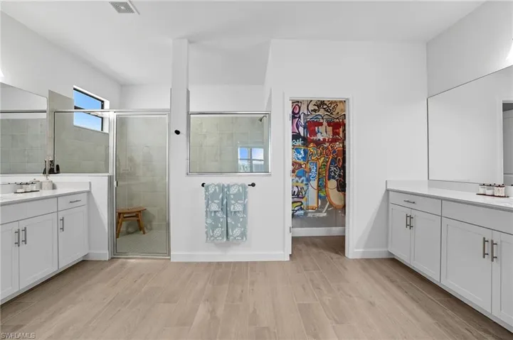 Full bathroom with two vanities, a stall shower, wood finish floors, and a walk in closet