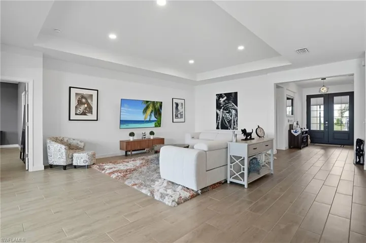 Living area featuring a raised ceiling, wood finish floors, recessed lighting, and french doors