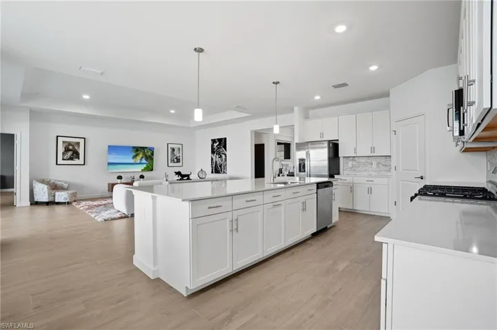 Kitchen featuring white cabinets, pendant lighting, open floor plan, light wood finished floors, and recessed lighting