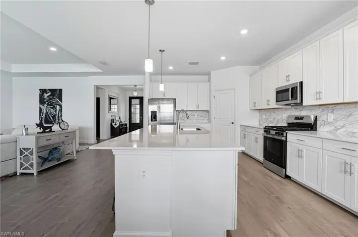 Kitchen with appliances with stainless steel finishes, light wood-type flooring, white cabinetry, decorative light fixtures, and recessed lighting