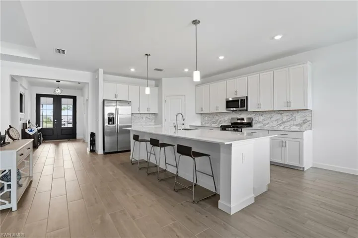Kitchen with a breakfast bar, white cabinets, a kitchen island with sink, tasteful backsplash, and recessed lighting
