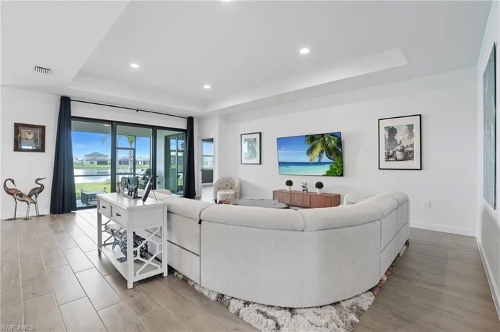 Living area with a tray ceiling, recessed lighting, and light wood-type flooring