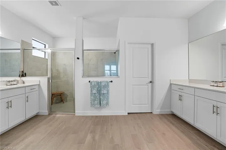 Full bathroom with a shower stall, two vanities, and light wood-style floors