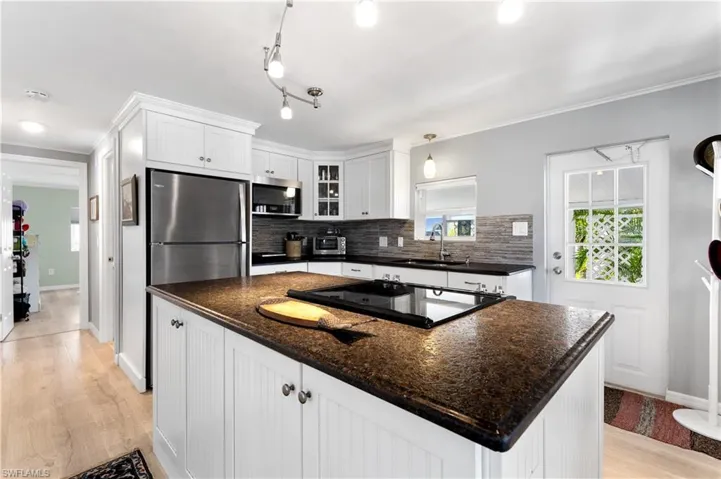 Kitchen featuring white cabinetry, light wood-style floors, a kitchen island, decorative backsplash, and ornamental molding