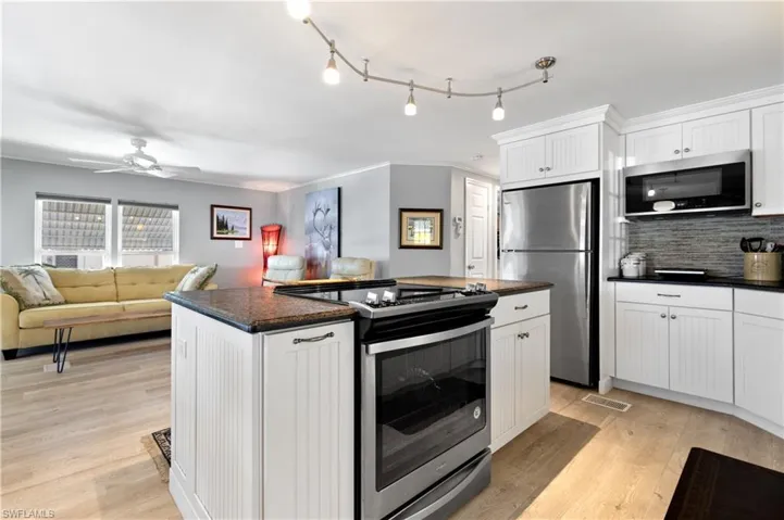 Kitchen with open floor plan, stainless steel appliances, white cabinets, light wood finished floors, and ornamental molding