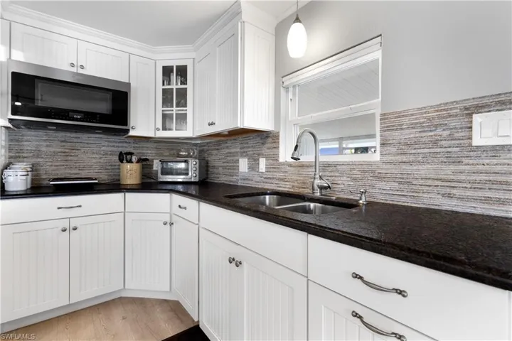 Kitchen featuring tasteful backsplash, white cabinets, stainless steel microwave, dark stone counters, and glass insert cabinets