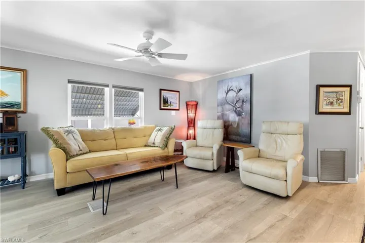 Living room with wood finished floors, ceiling fan, and crown molding