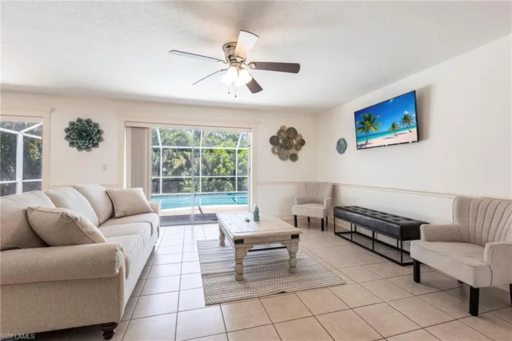 Living room with ceiling fan, a sunroom, light tile patterned floors, and a textured ceiling