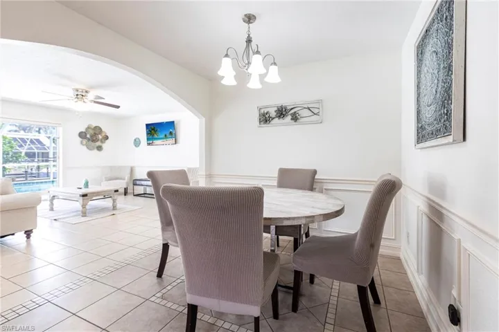 Dining area with a wainscoted wall, ceiling fan, a chandelier, light tile patterned floors, and arched walkways