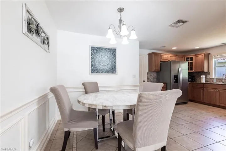Dining room with hanging lights, wainscoting, a decorative wall, and light tile patterned flooring