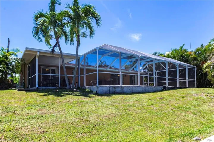 Rear view of house featuring a sunroom, glass enclosure, and a lawn